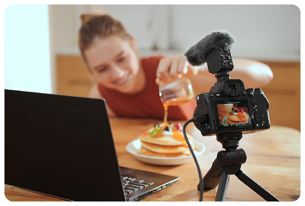 woman wearing muted oragne knitted vest Pouring syrup on pancakes live vlogging with Sony A7 IV camera and laptop